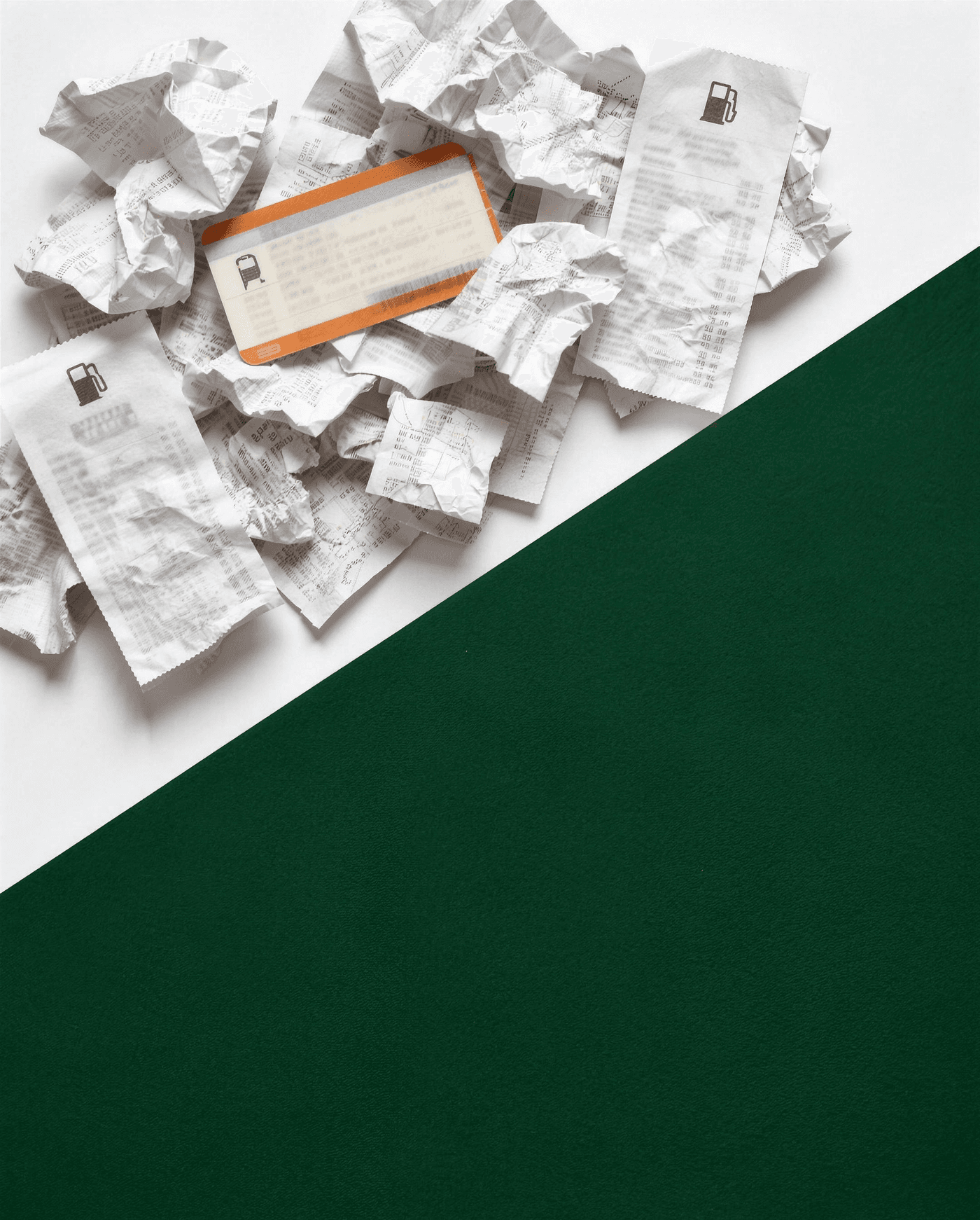 A heap of crumpled receipts, a train ticket and fuel receipts on white, cut diagonally by a clean dark green surface